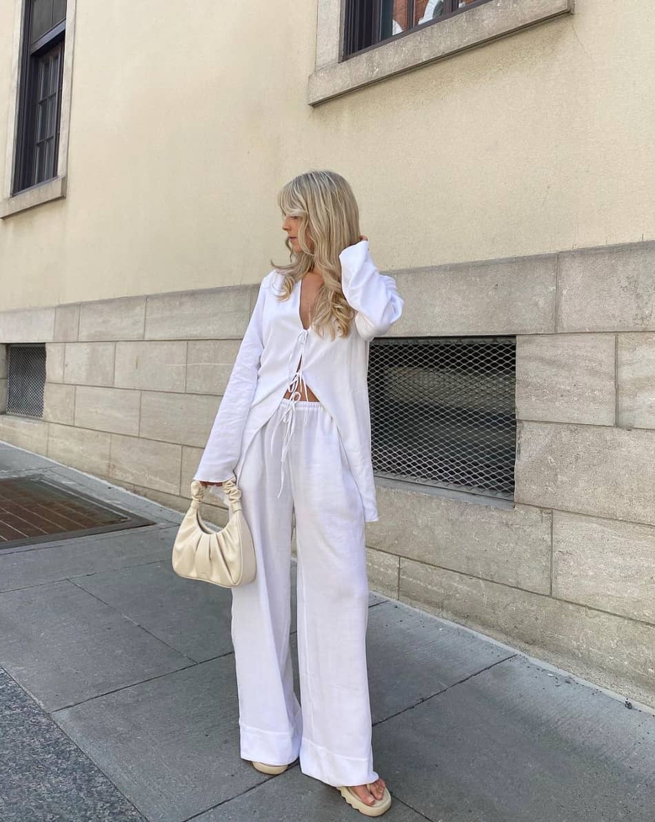 An image of a woman with white linen pants and an oversized white tie top