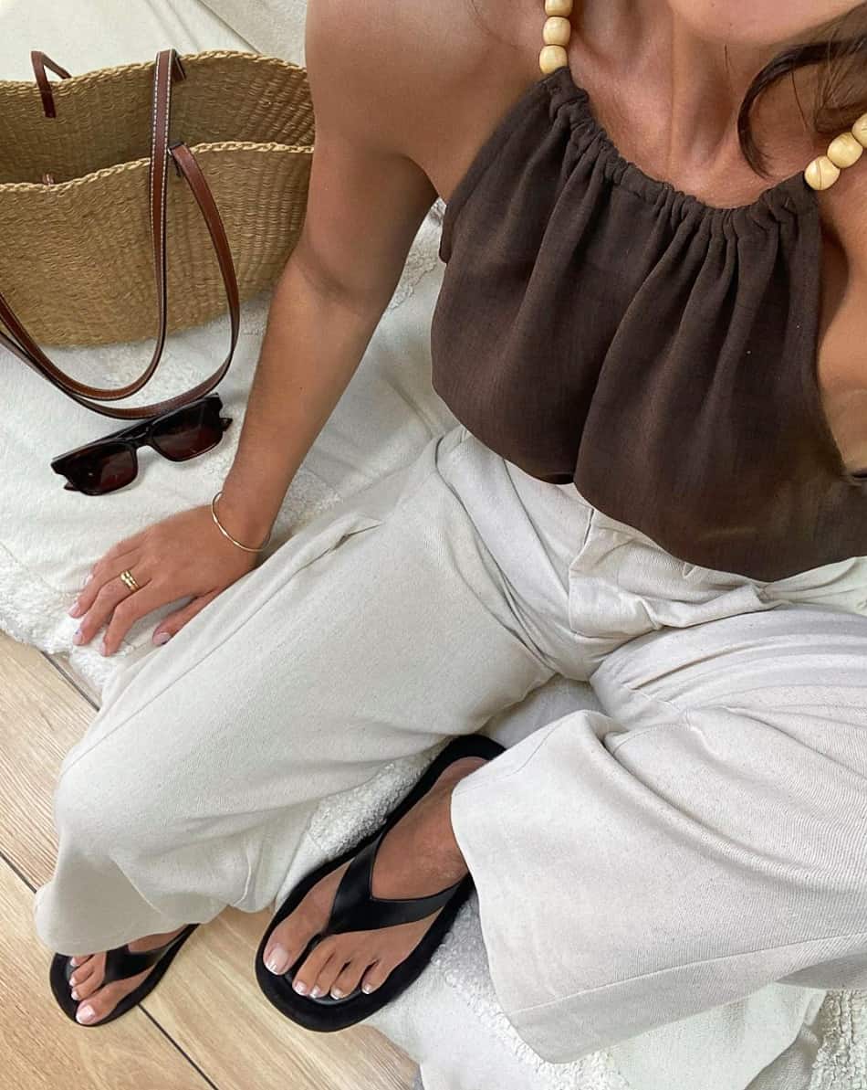 An image of a woman with light grey linen pants, a brown halter top, and black flip flops