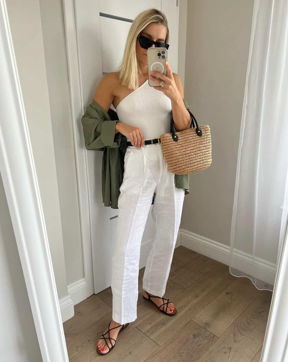An image of a woman with white linen pants, an asymmetrical white tank, a green button-up, and strappy black sandals