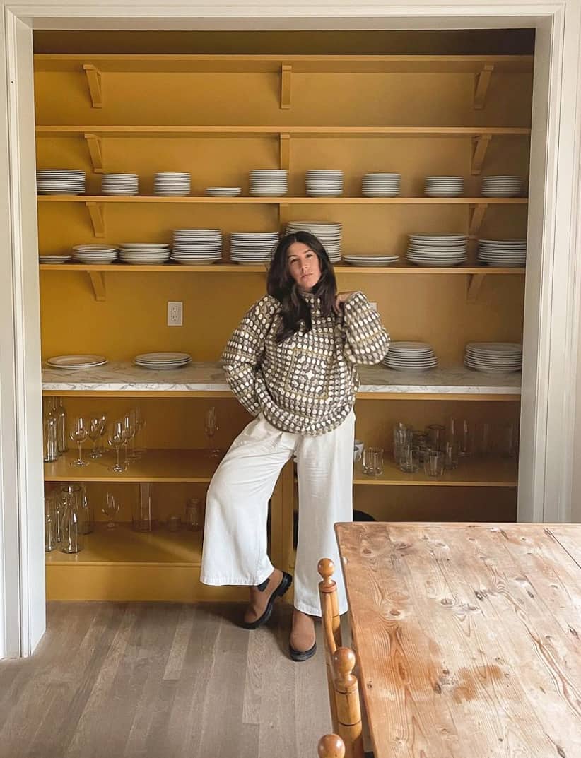 An image of a woman with white linen pants, an oversized sweater, and brown boots