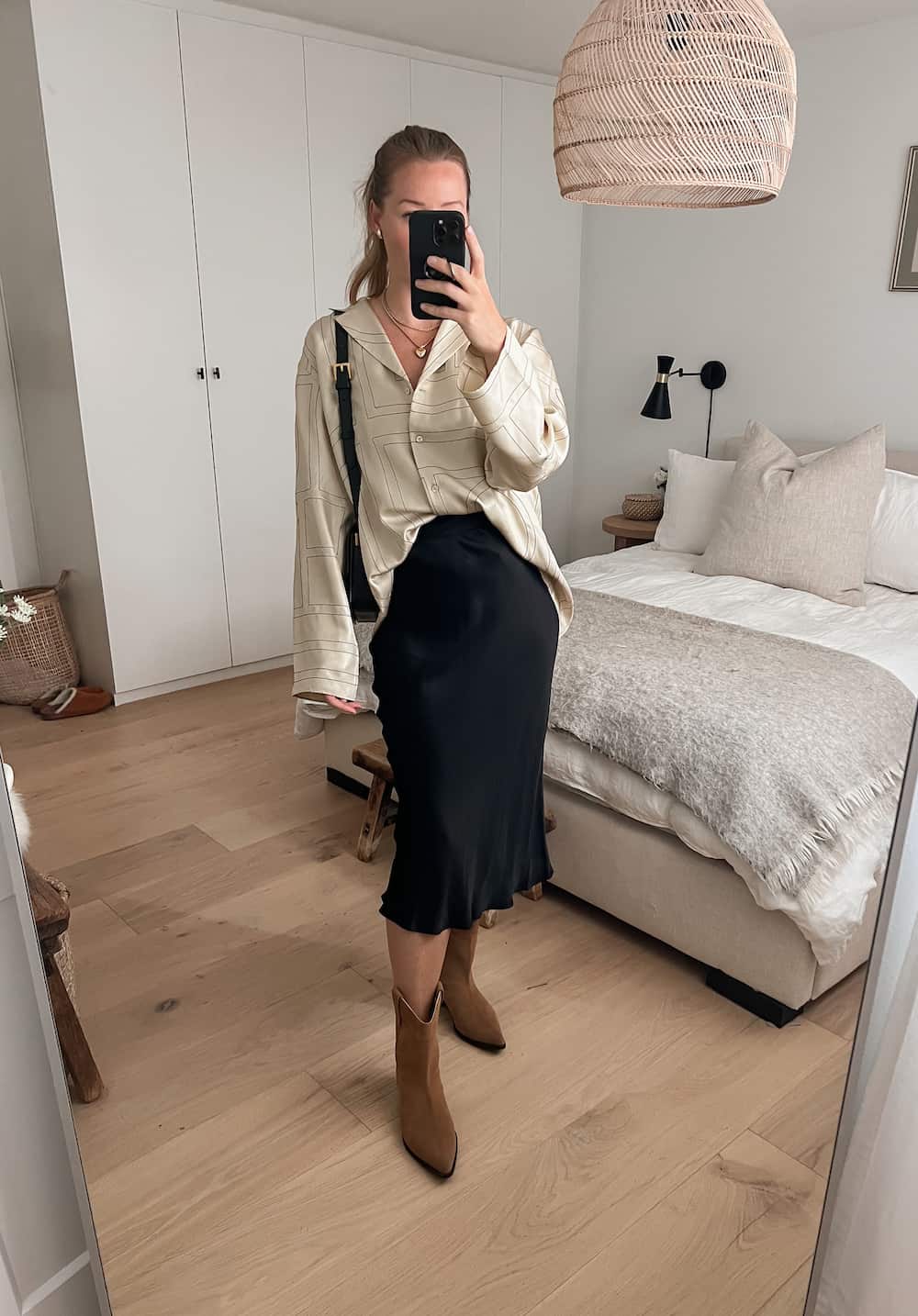 woman wearing a silk Toteme shirt with a silk midi slip skirt in black, western style boots for a Nashville outfit 