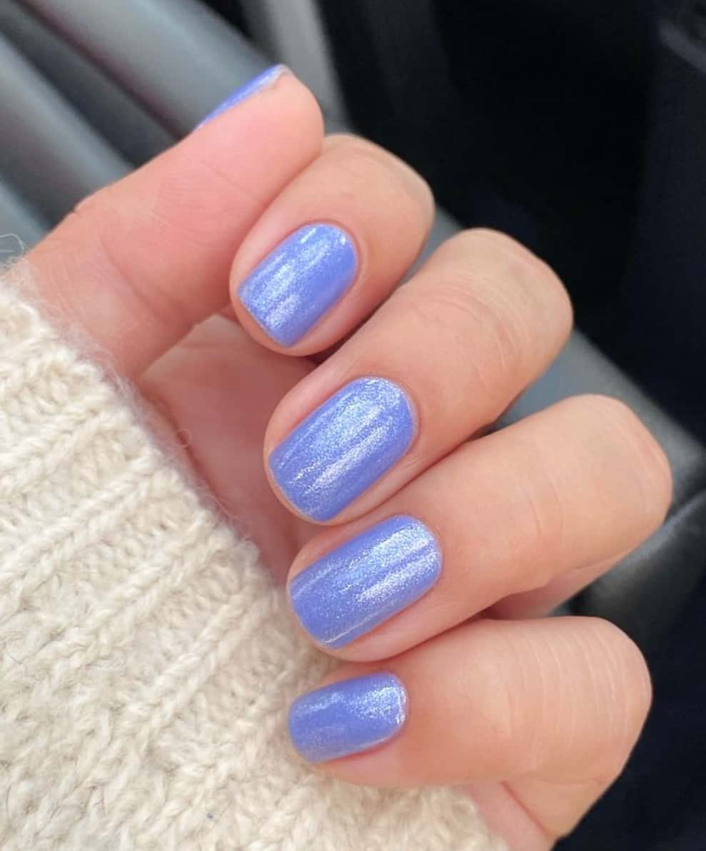 A hand with short square nails with shimmering lavender blue polish