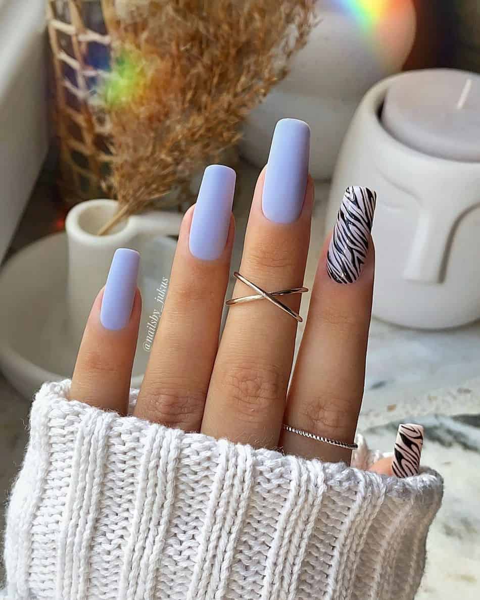 A hand with long square nails featuring matte periwinkle polish and zebra accent nails