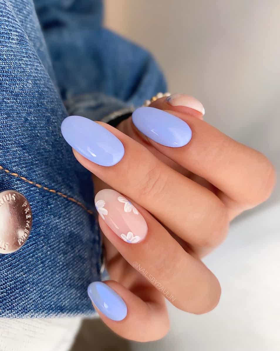 A hand with periwinkle polish and nude accent nails with white flowers