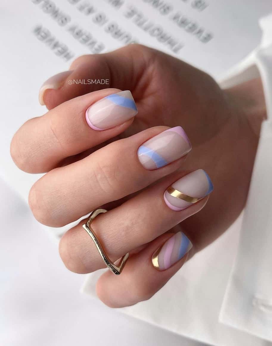 A hand with nude nails with pink, lavender blue, and gold accent stripes