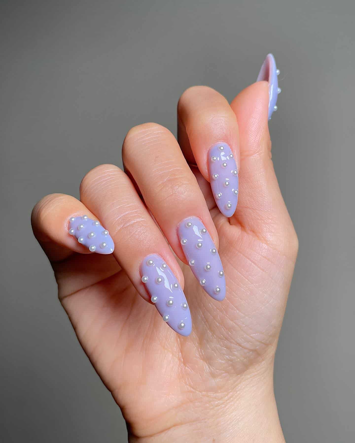 A hand with long solid-colored periwinkle nails and pearl accent beads