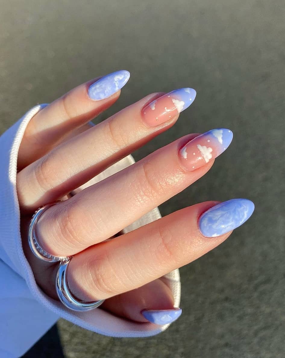 A hand with white and periwinkle marbled nails and nails with periwinkle ombre and white clouds
