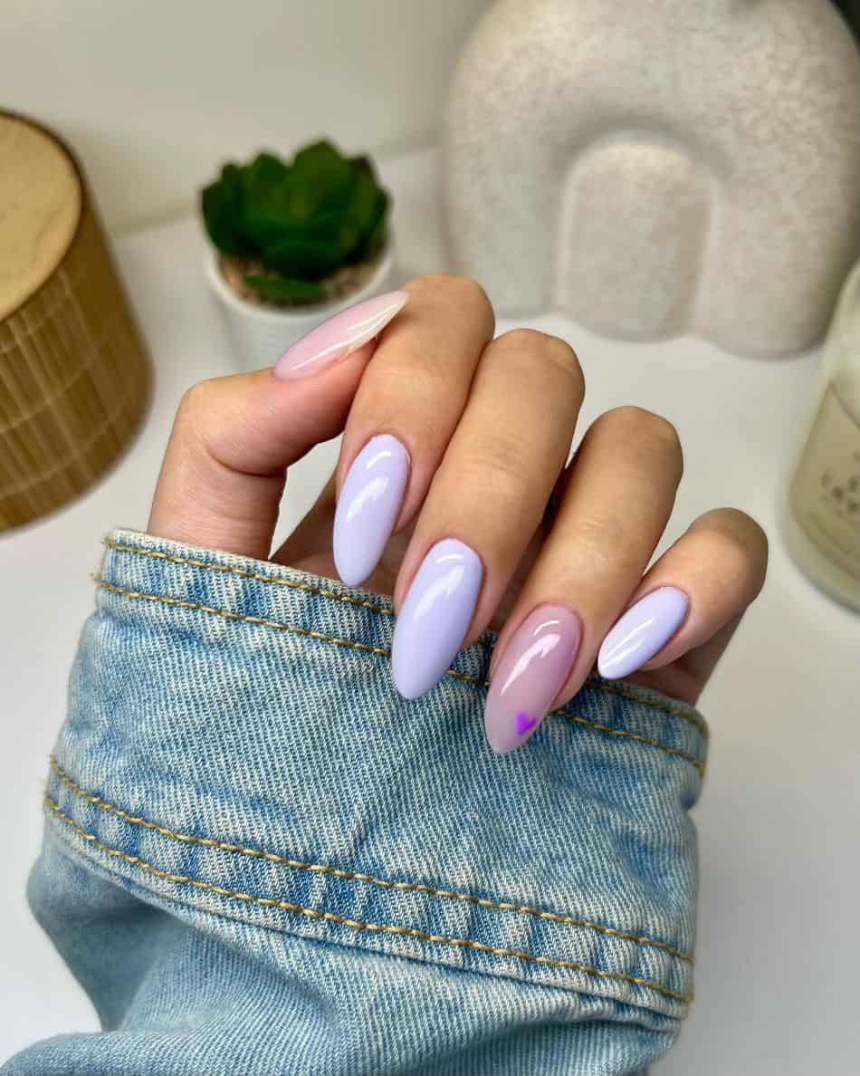 A hand with long almond nails featuring solid lavender blue polish and nude pink accent nails with a purple heart