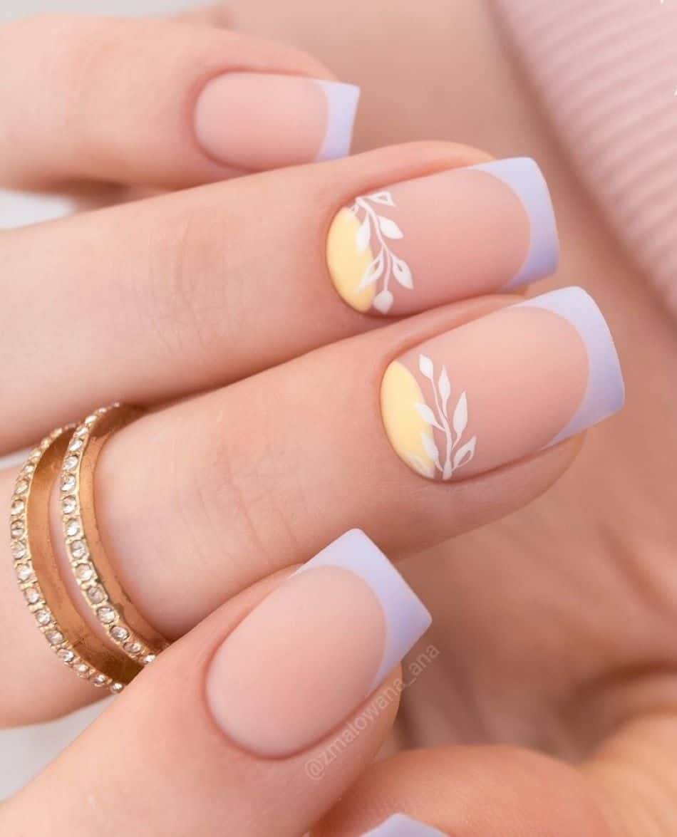 A hand with periwinkle French tips and accent nails with yellow half moons and white leaf art