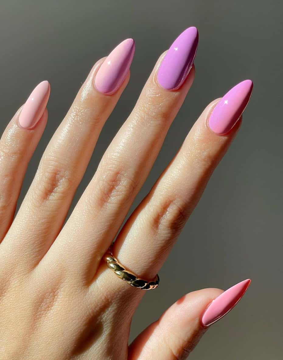 An image of a hand with almond nails featuring a purple and pink ombre design