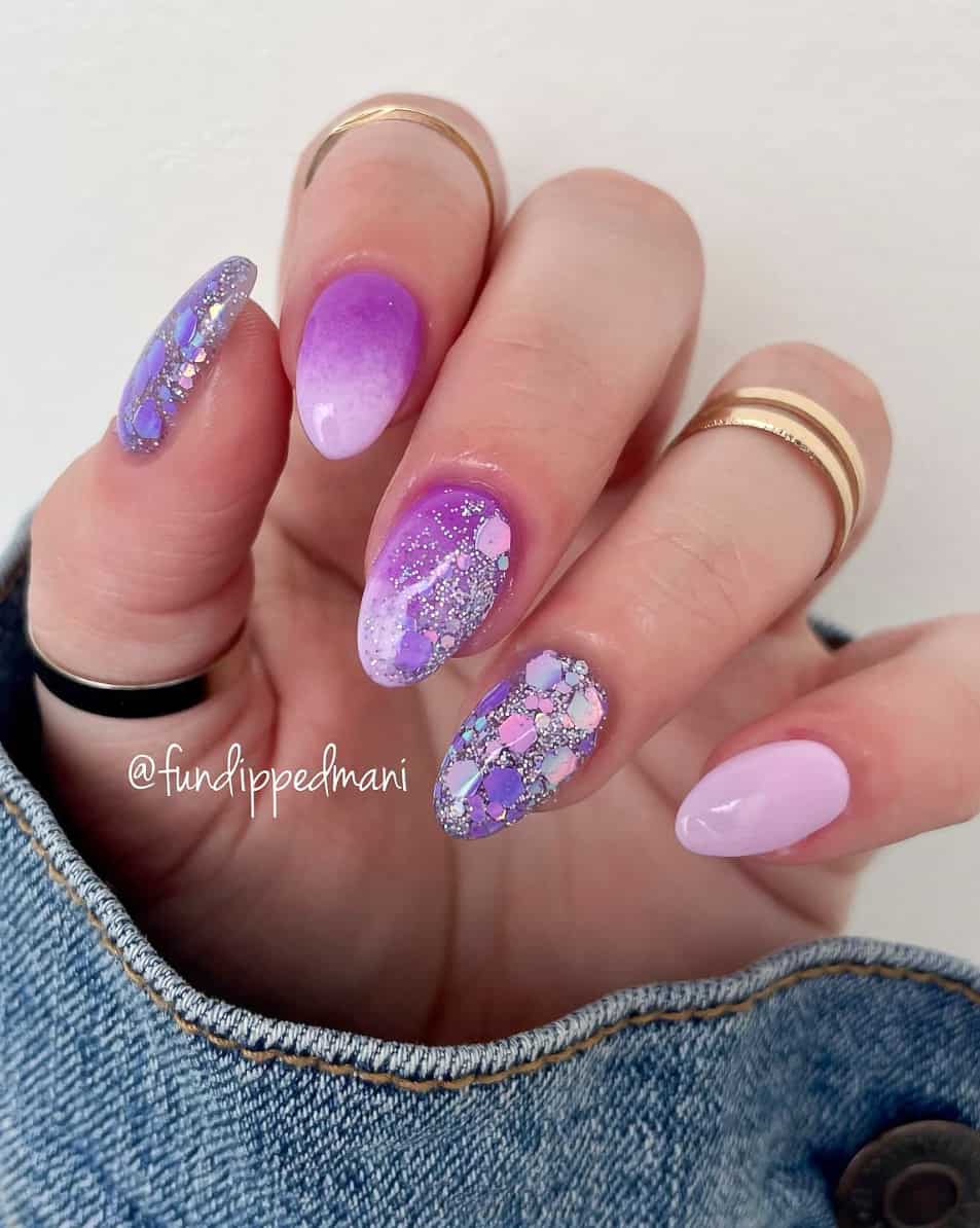 An image of a hand with a purple ombre manicure and glitter accent nails
