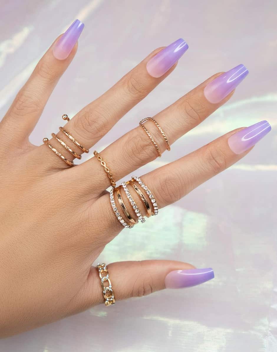 An image of a hand with long square nails featuring nude to lavender ombre