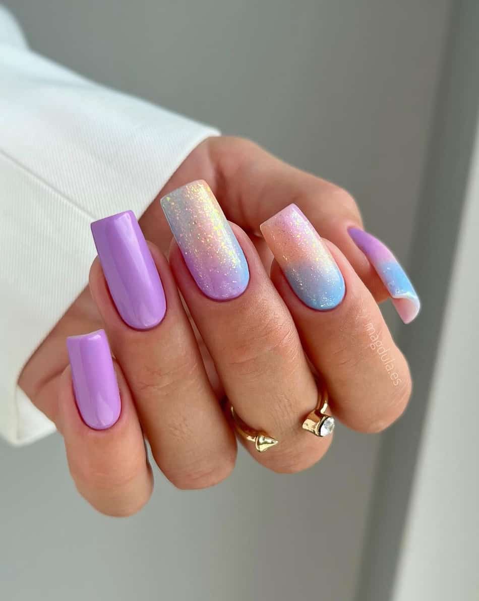 An image of a hand with rainbow glitter and lilac ombre with solid-colored purple accent nails