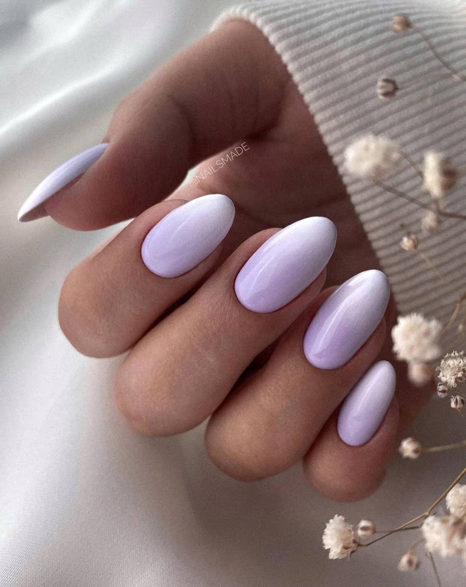 An image of a hand with white and pastel purple ombre on round nails