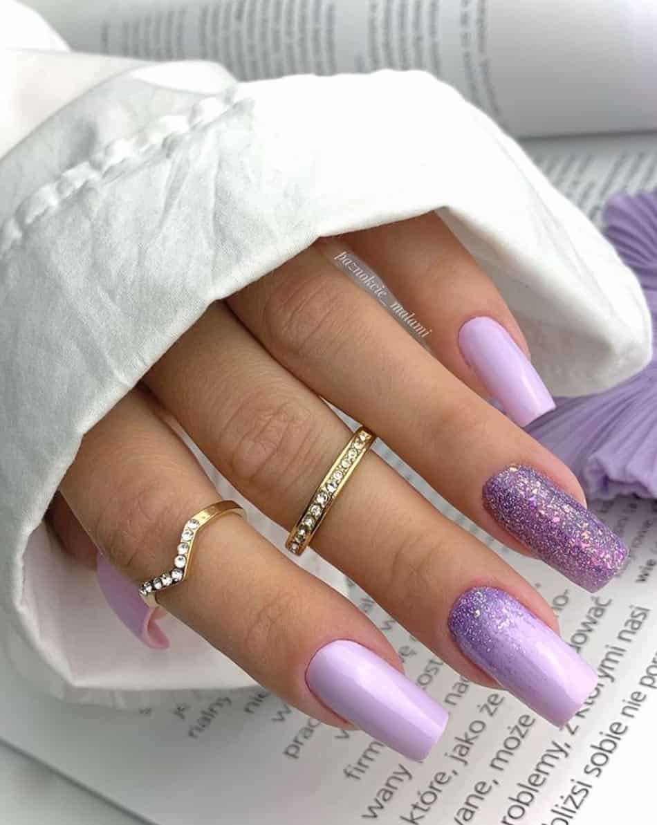 An image of a hand with lilac nails and lilac glitter ombre
