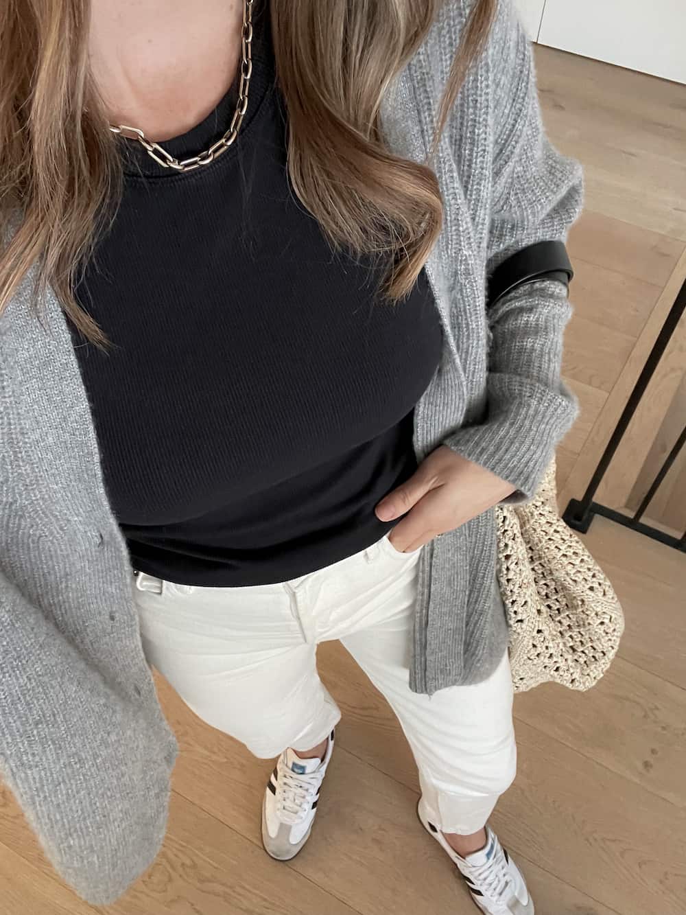 woman wearing a spring capsule wardrobe outfit with a grey knit cardigan, black top, off-white jeans, and white sneakers