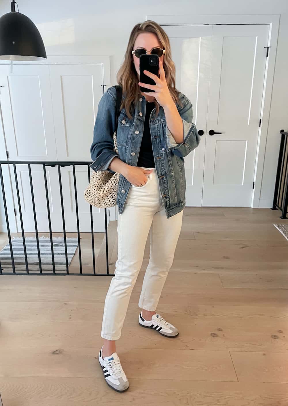 woman wearing a spring capsule wardrobe outfit with an oversized denim jacket, black top, off-white jeans, and white sneakers