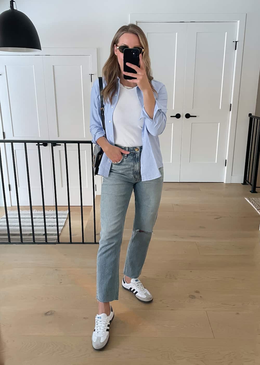 woman wearing a spring capsule wardrobe outfit with a blue button down shirt over a white tank with blue jeans and white sneakers