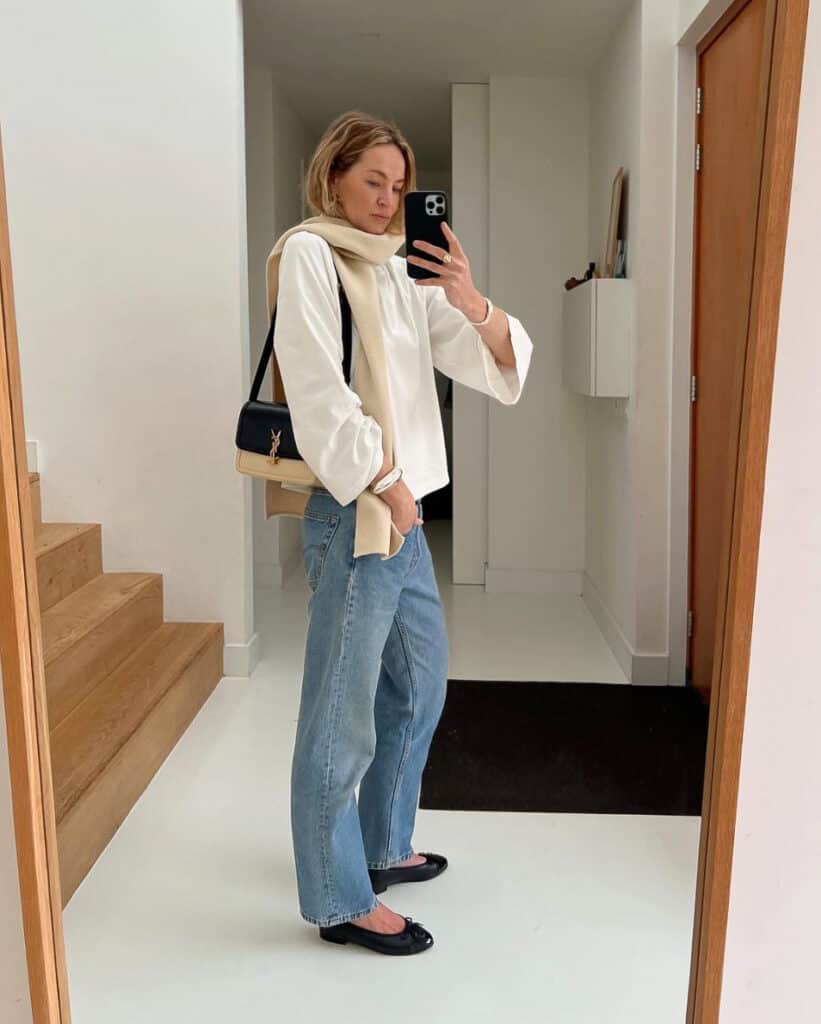 woman wearing a long sleeve white top with a scarf and blue jeans with ballet flats and a YSL Solferino bag