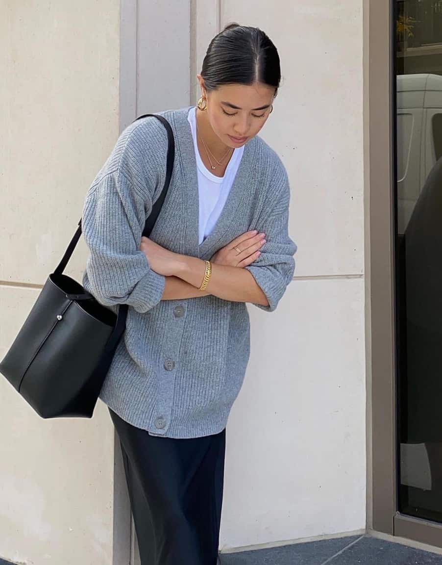 woman wearing and oversized grey knit cardigan with a black tote bag and black midi skirt