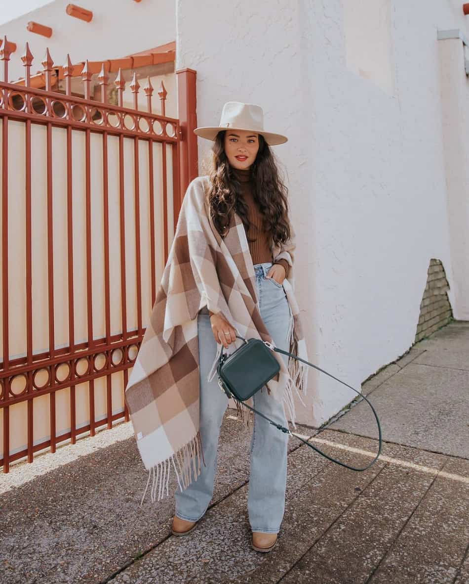 woman wearing a fedora hat, poncho, jeans, and cowboy boots