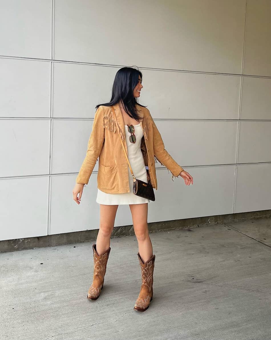 woman wearing a mini dress with a tan suede jacket and brown cowboy boots