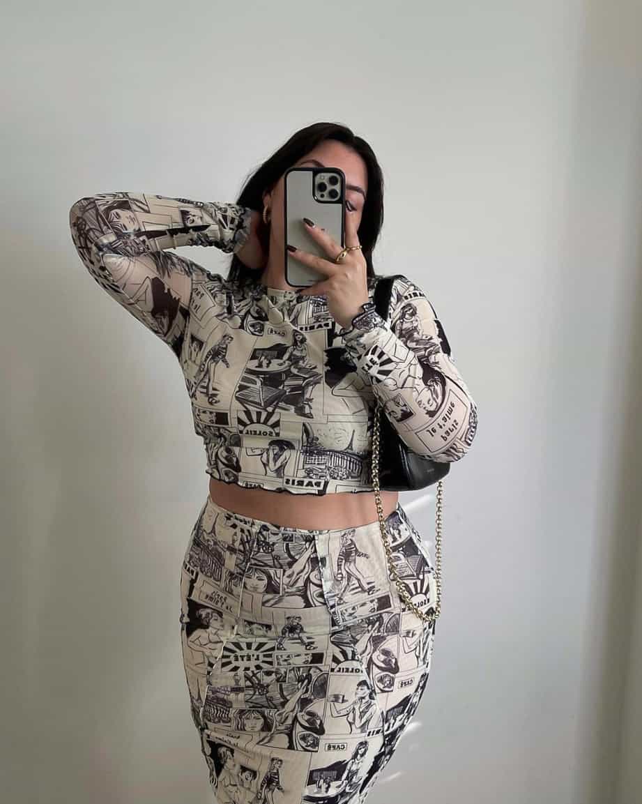 A woman wearing a matching skirt and crop top set featuring a black and white comic print and a black shoulder bag