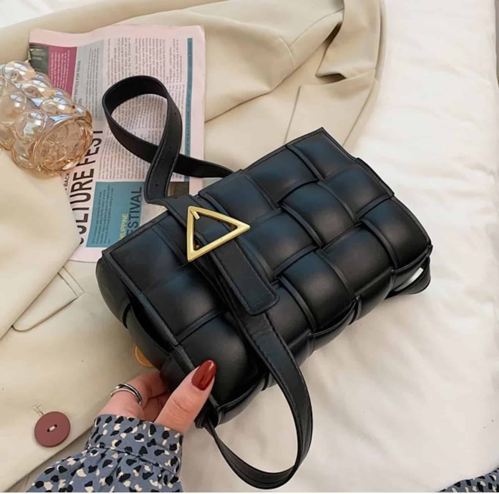 a black bag with woven vegan leather and a triangle gold buckle on the strap