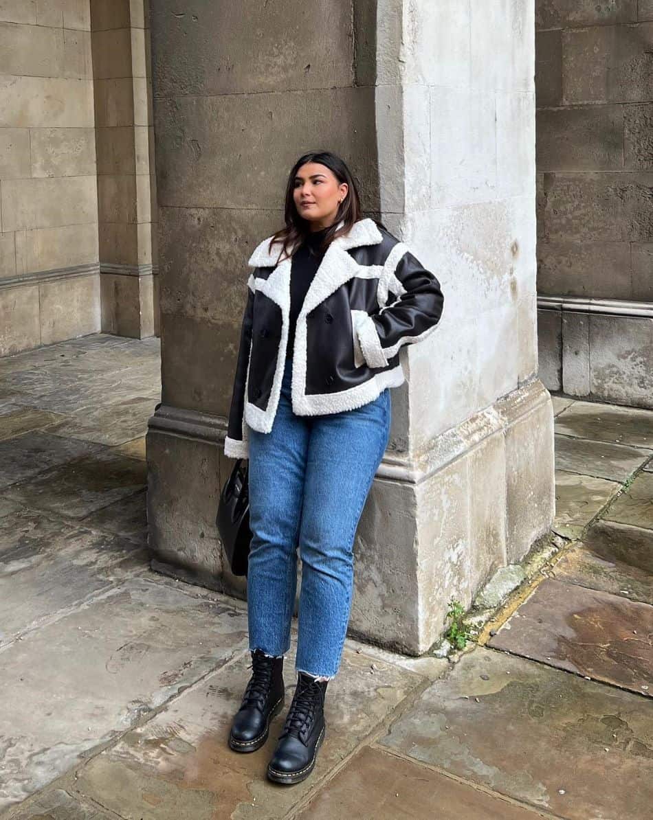 A woman wearing blue jeans, black boots, and a black and white sherpa jacket