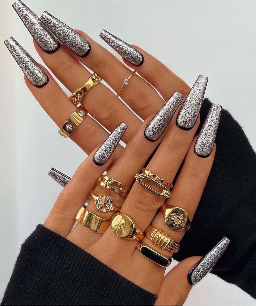 A hand with long coffin nails with a glittery silver polish and black outlines