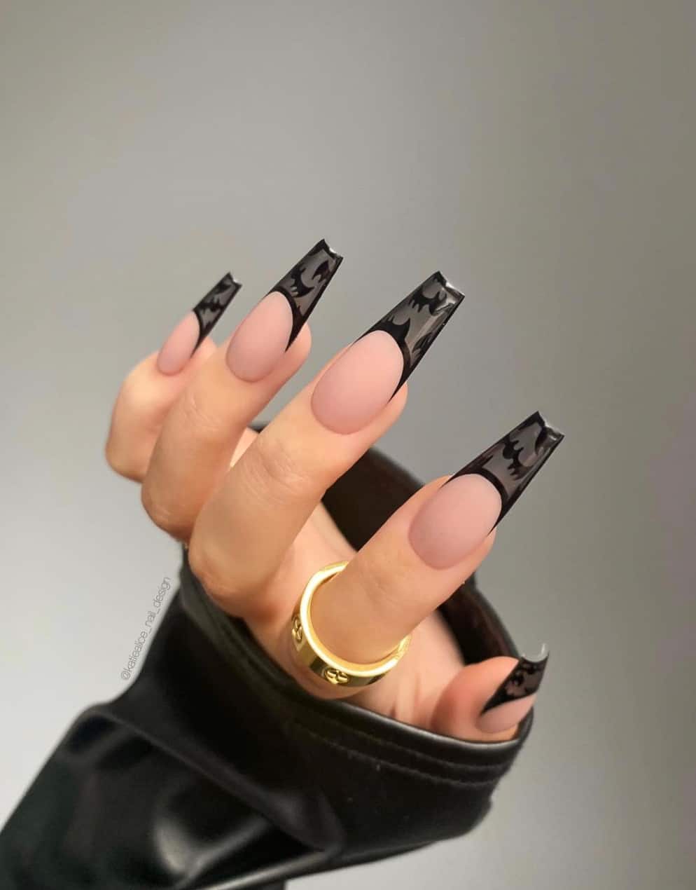 A hand with coffin shaped nude nails and black French tips with bat nail art