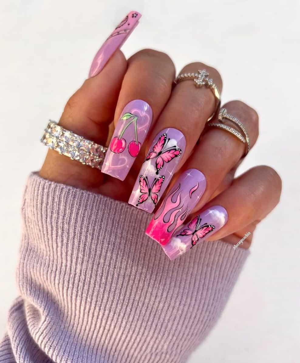 A hand with square purple collage nails featuring pink flames, cherries, and pink butterflies