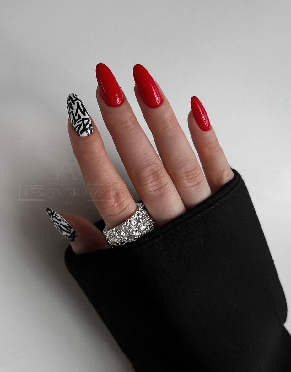 A hand with red almond nails and two white accent nails with black graffiti style letters