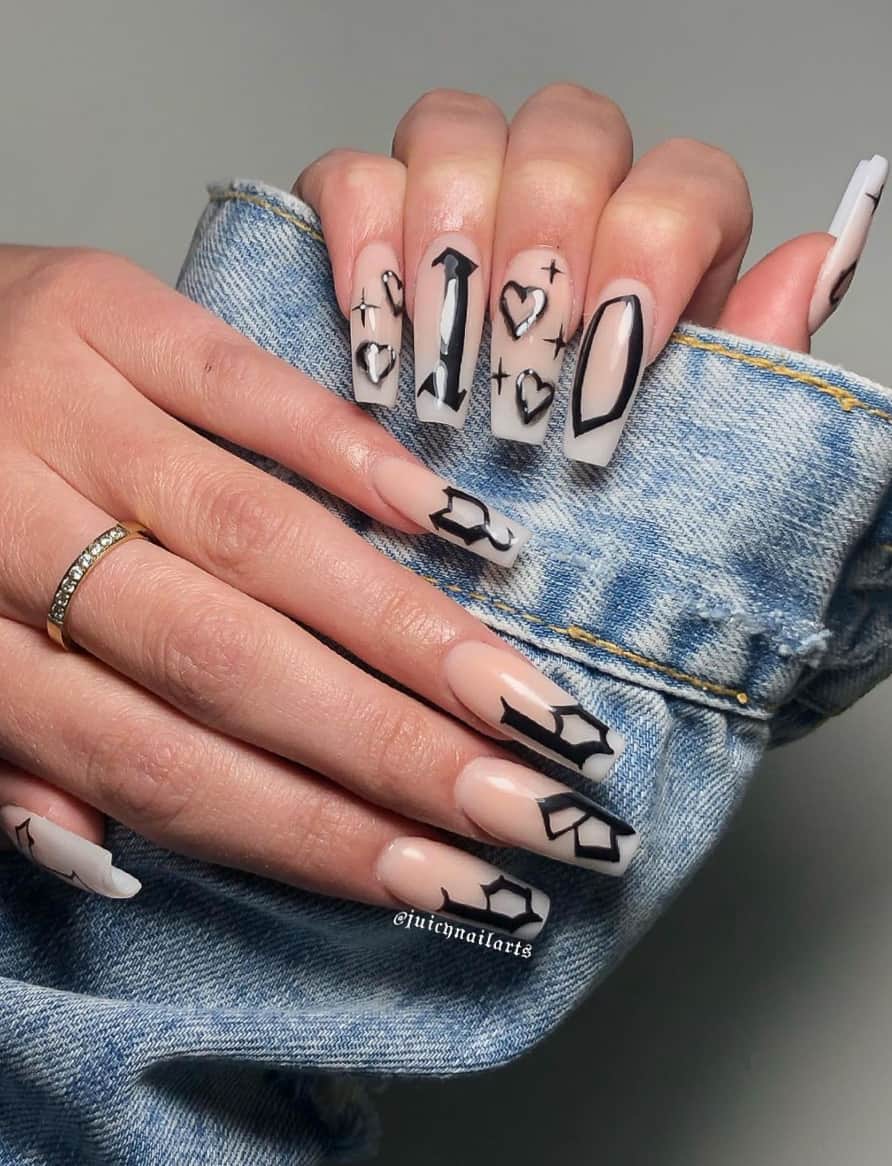 A hand with nude and white ombre nails with black gothic letters, hearts, and sparkles