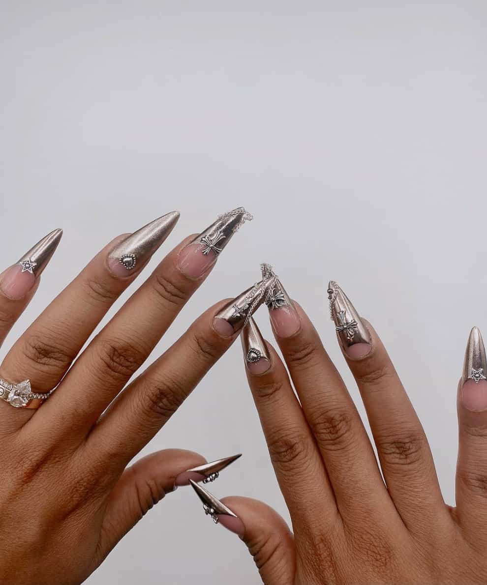 A hand with long stiletto nails featuring silver chrome French tips and bead accents