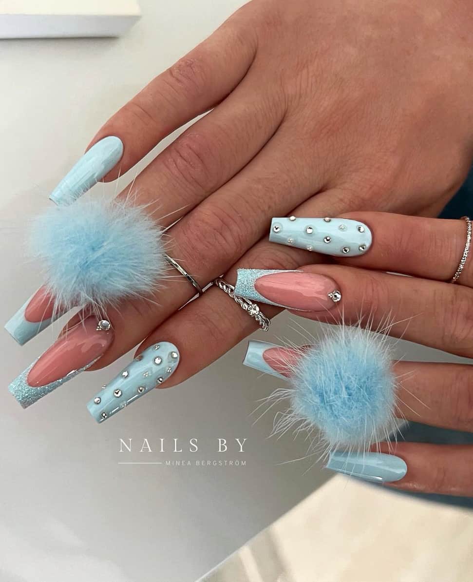 A hand with medium coffin nails featuring solid-colored nails and French tips in baby blue polish with glitter and gem accents