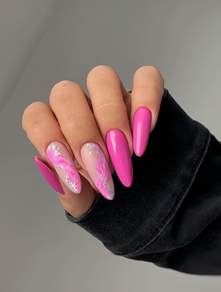 A hand with bright pink almond nails and two accent nails with nude polish, pink and white marbled strips, and silver glitter