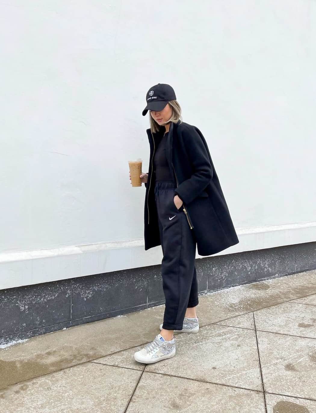 Woman wearing a black hat, jacket, and pants with Golden Goose sneakers