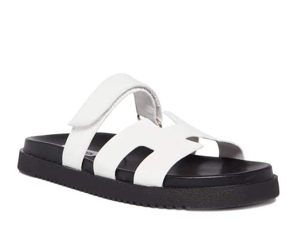 Image of a white sandal with H cut out detail and black sole, a dupe of the Hermes chypre sandal