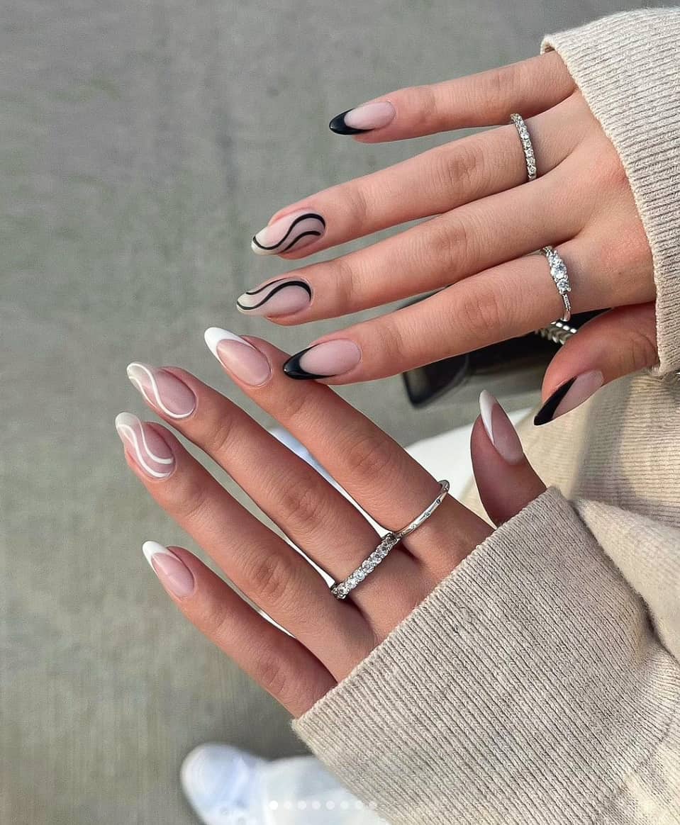 A hand with nude almond nails with black French tips and wavy line accents on one hand and white on the other