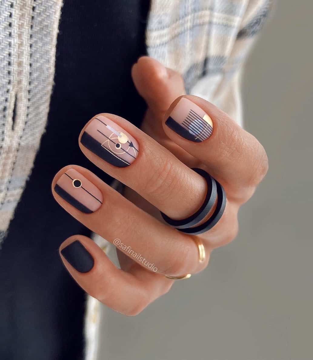 A hand with short matte nude nails with black geometrical line art and gold accents