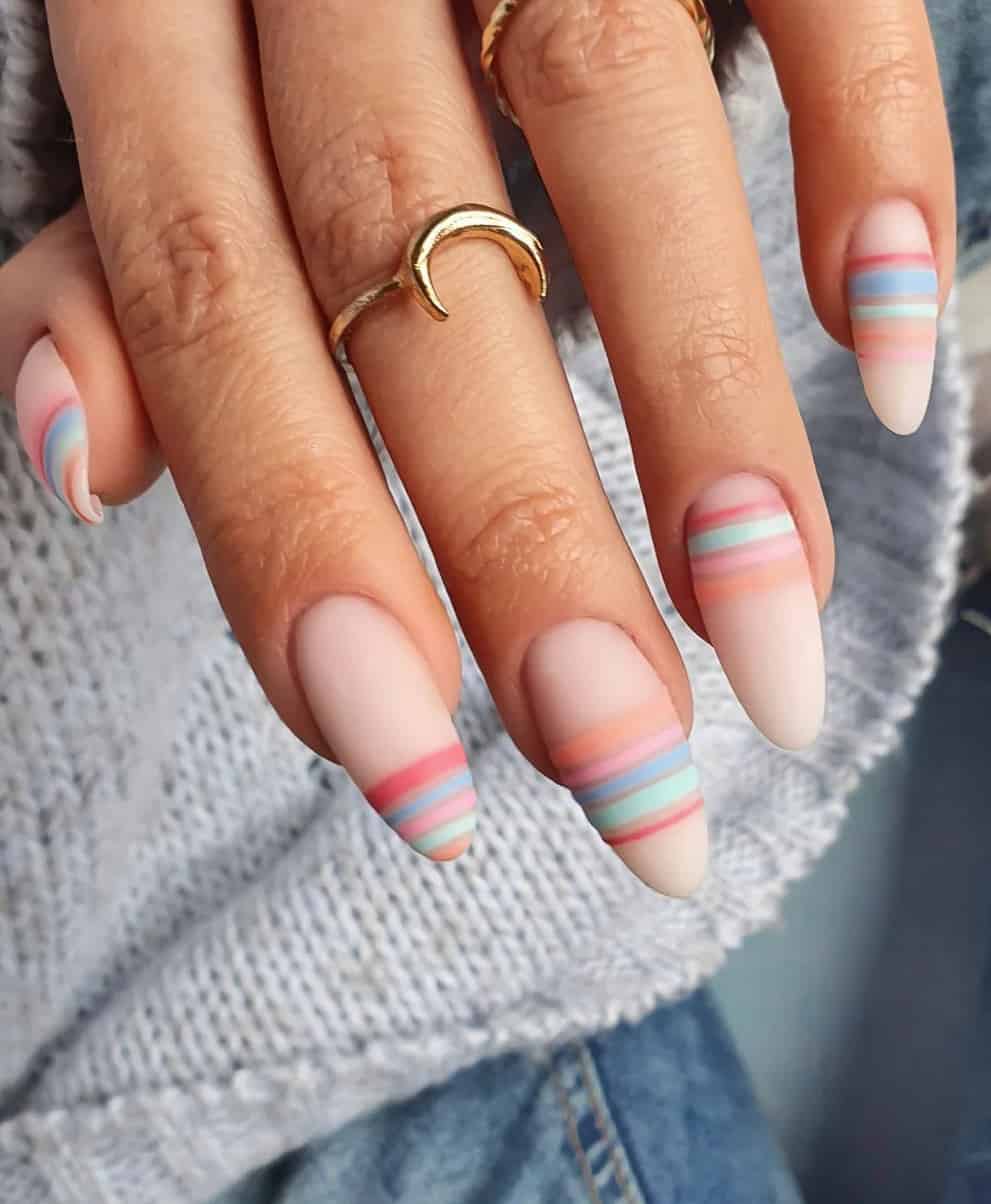 A hand with matte nude pink almond nails and colorful pastel horizontal lines