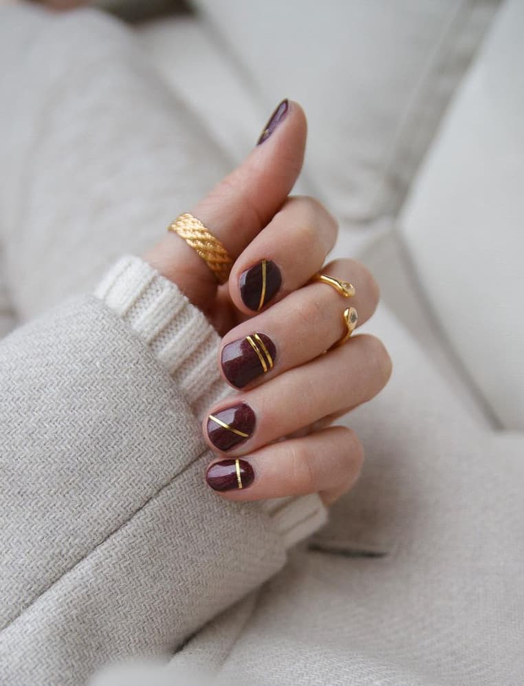 A hand with short mahogany nails with gold accent lines