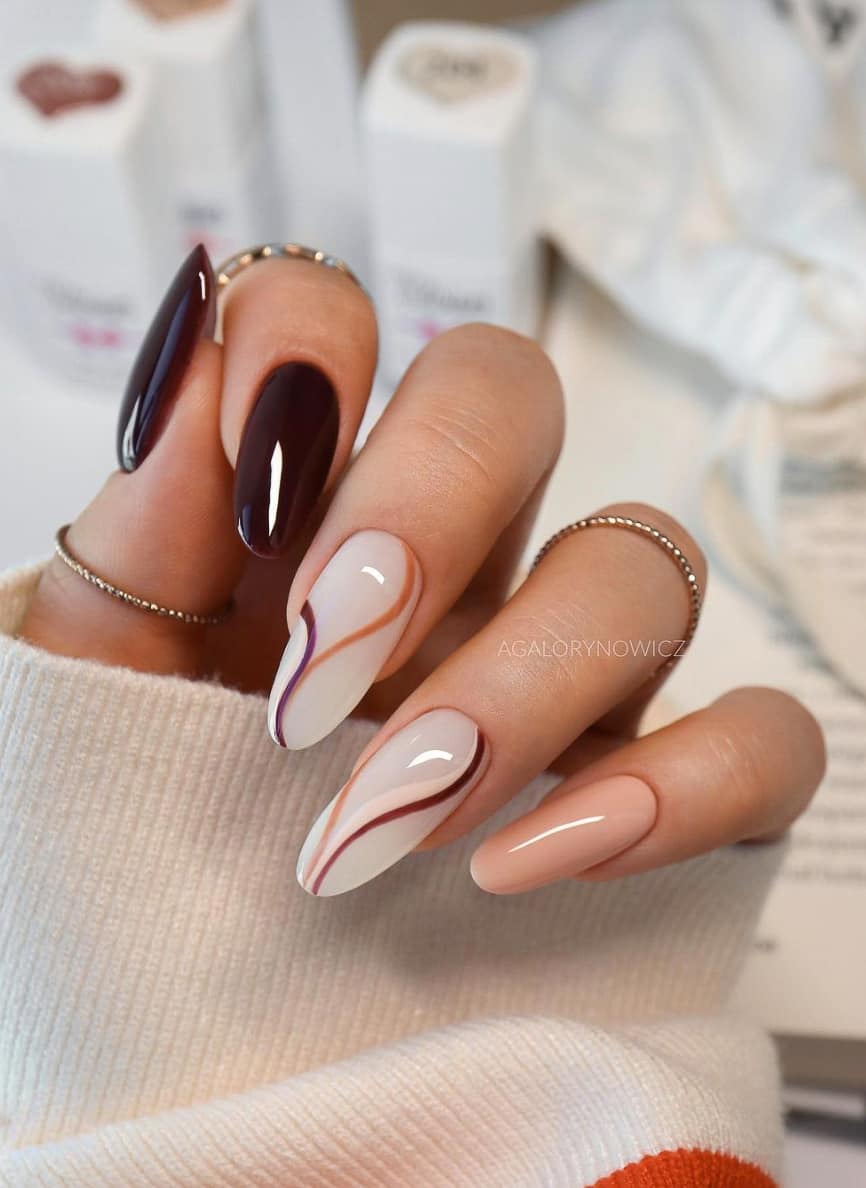 A hand with milky white, beige, and dark brown almond nails with brown and beige accent lines