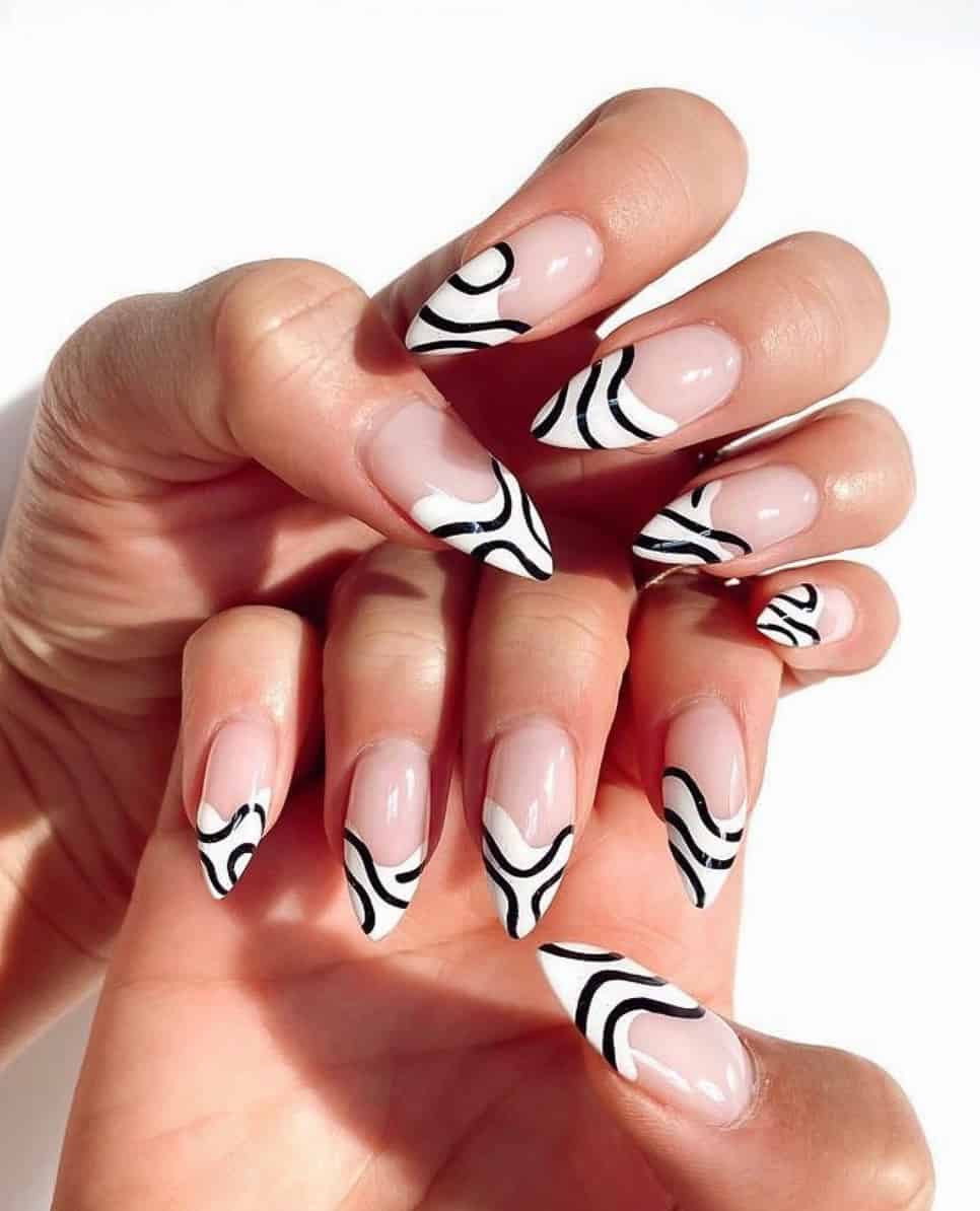 A hand with nude stiletto nails with white French tips and black wavy line accents