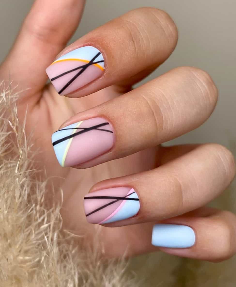A hand with short square nails with a matte nude base polish, pastel blue accents, and a combination of colorful and black line details