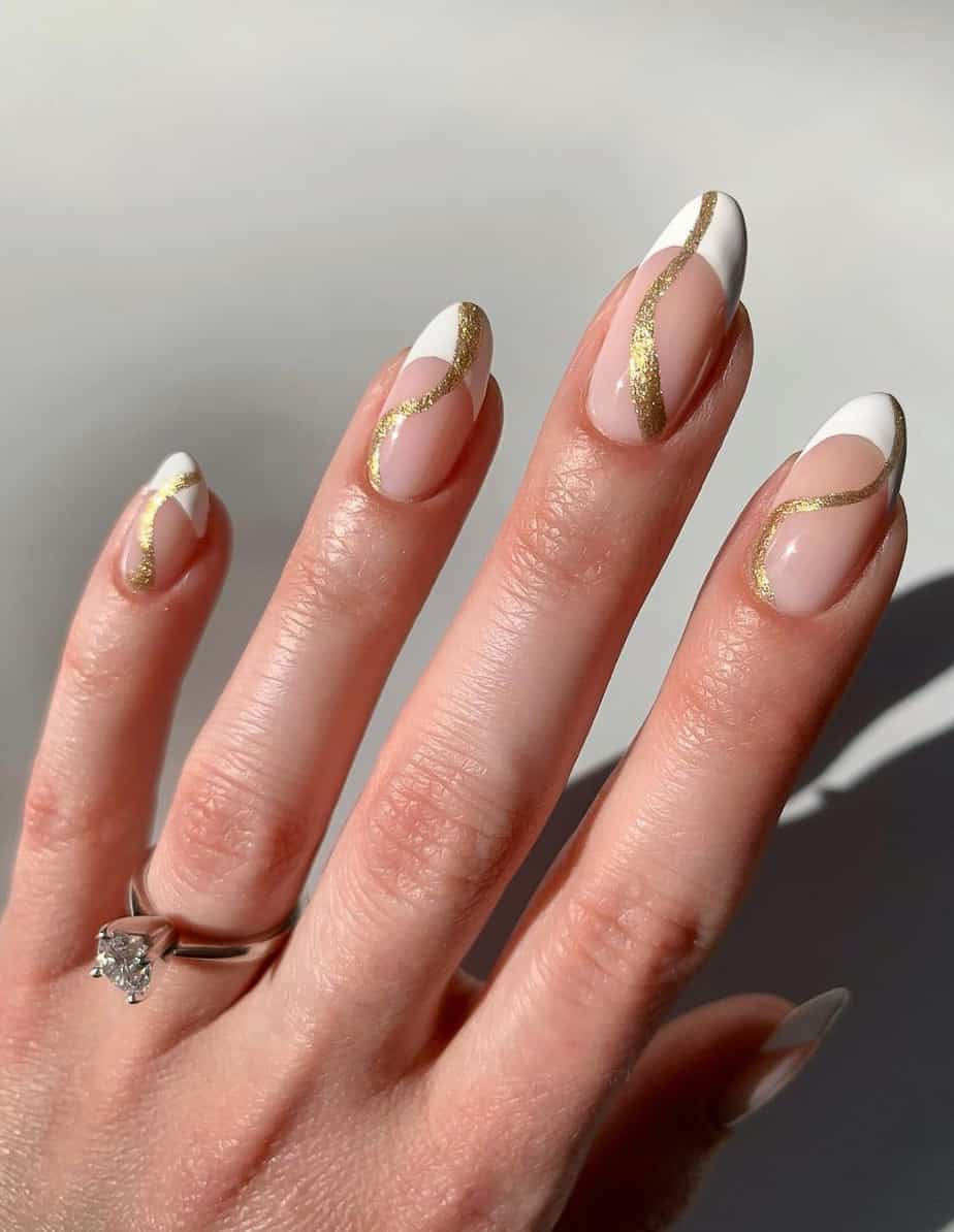 A hand with nude almond nails painted with white French tips and gold wave accent lines
