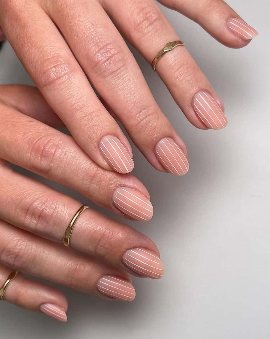 A hand with short nails painted with nude polish, vertical white accent lines, and a matte finish