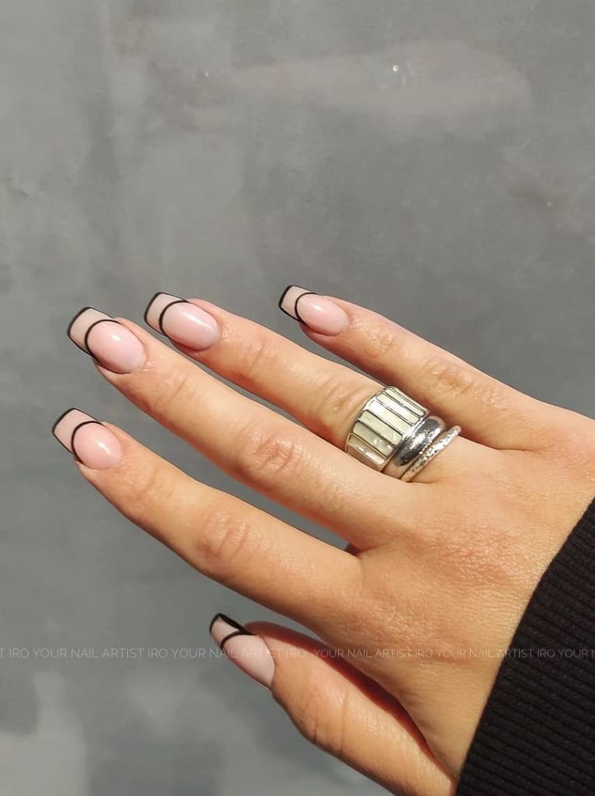 A hand with nude square nails featuring black French tip outlines