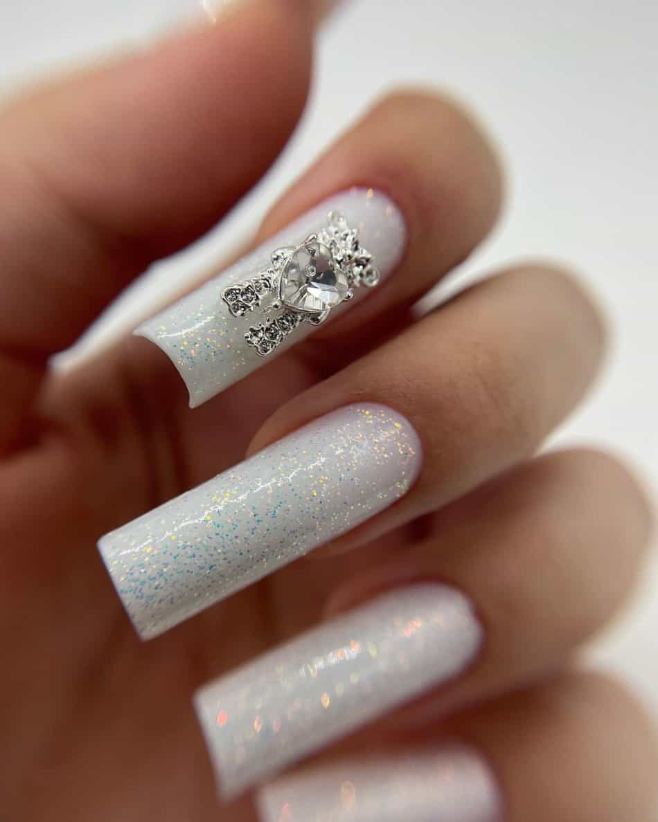 A hand with long square nails with glittery white polish and gem details